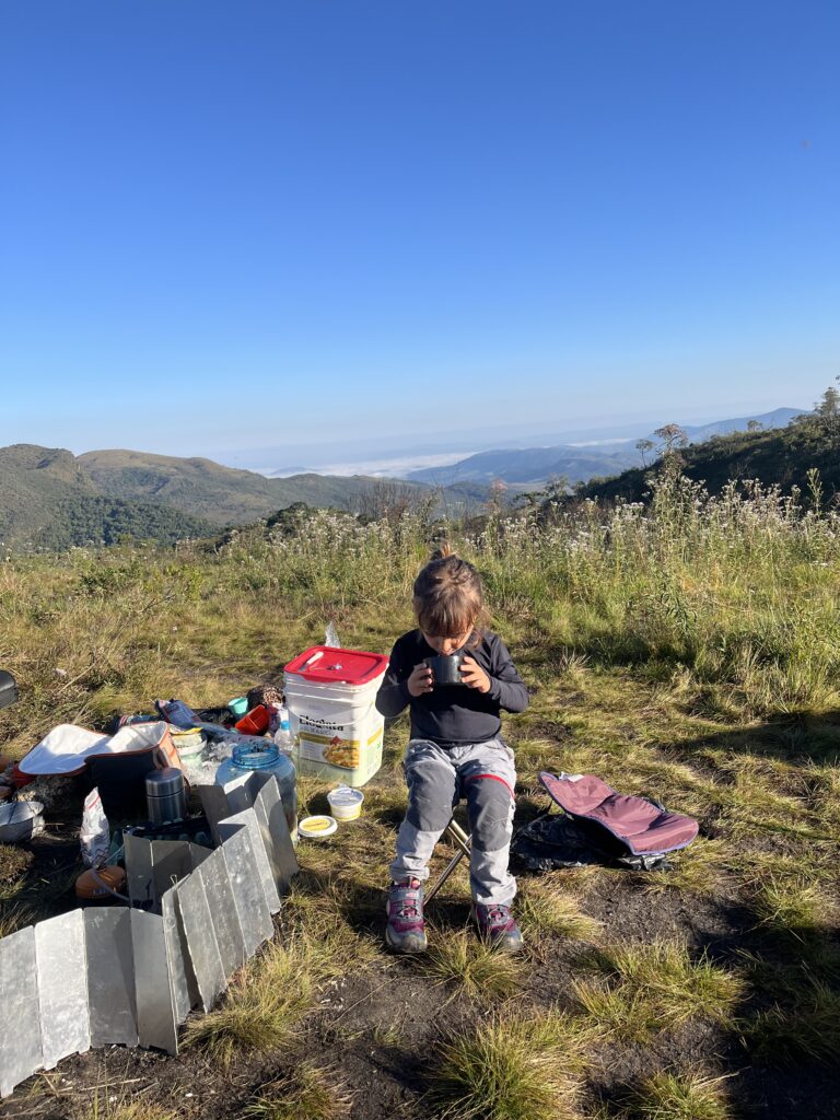 Criança sentada tomando algo quente em caneca durante acampamento na montanha