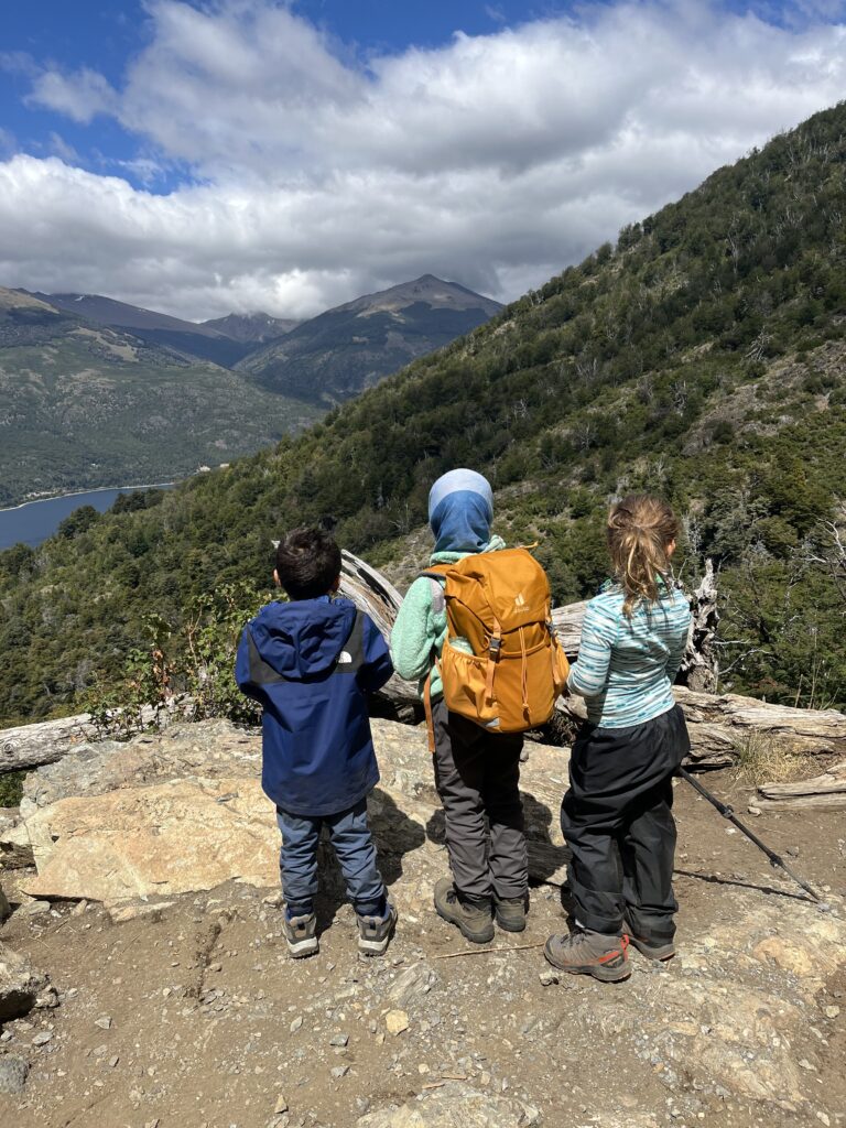 Crianças paradas observando vista de montanhas e lago