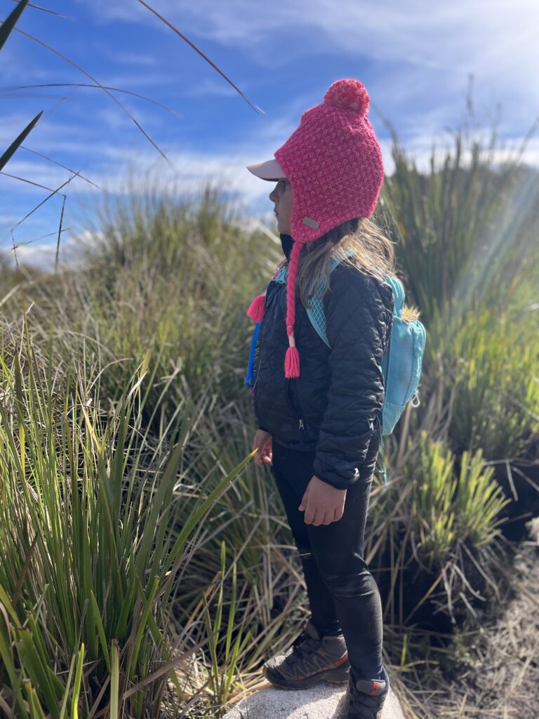 Menina de gorro rosa observando a paisagem em trilha de montanha